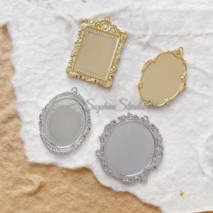 May include: Four decorative metal pendants in various shapes and finishes. There is one rectangular gold pendant, one oval gold pendant, one oval silver pendant, and one round silver pendant, all featuring intricate ornate filigree borders.