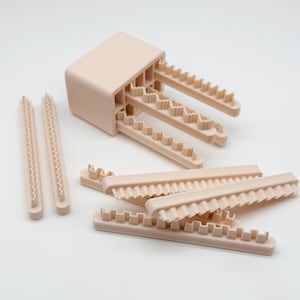 May include: A set of light beige plastic clay cutters featuring a rectangular block with multiple protruding, wavy-edged blades, alongside several individual straight, serrated-edge strips designed for creating textured patterns in modeling clay.