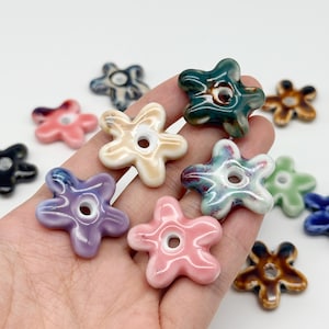 Peut inclure: Une collection de petites perles en forme de fleur à cinq pétales avec un trou central. Les perles présentent une finition brillante et émaillée dans diverses couleurs, dont le rose, le violet, le vert, le marron et le bleu, avec des effets marbrés.