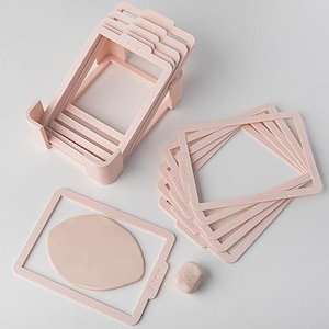 Puede incluir: Un conjunto de guías rectangulares de color rosa claro para el grosor de la arcilla con medidas de profundidad variadas etiquetadas 1mm, 1.5mm, 2mm, 2.5mm, 3mm, 3.5mm, 4mm, 4.5mm y 5mm. Incluye un soporte, varios marcos sueltos y arcilla.