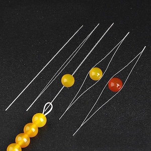 May include: Close-up of jewelry-making supplies. The image shows several strands of clear beading thread with yellow and red beads. Some threads are strung with beads, while others are separate. The background is a solid black.