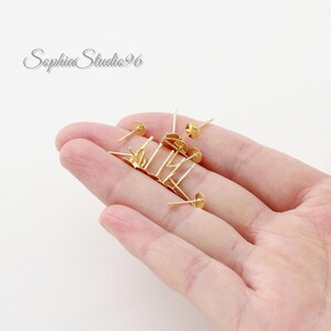 May include: A collection of small gold-toned metal earring studs with flat circular pads for attaching decorative elements. These jewelry findings feature thin posts and are designed for crafting custom earrings, presented in a bright metallic finish.