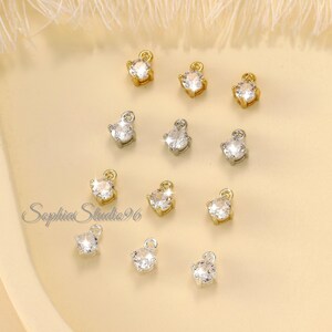 May include: A selection of small, sparkling cubic zirconia charms in gold and silver settings. Each charm features a clear, round stone and a small loop. The image includes the text "Sophia Studio 96".