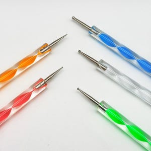 May include: A set of four dotting tools with clear acrylic handles containing internal colored spirals in orange, red, blue, and green. Each tool features a polished metal tip with a rounded ball end, designed for precision crafting and detailing.