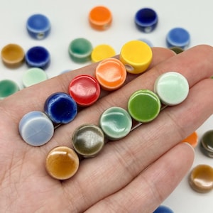 Könnte beinhalten: Eine Sammlung kleiner, runder, glasierter Keramikperlen in verschiedenen Farben wie Gelb, Orange, Rot, Blau, Grün und Braun. Die Perlen haben eine glatte, glänzende Oberfläche und ein einzelnes Loch, das an der Seite jedes Stücks sichtbar ist.