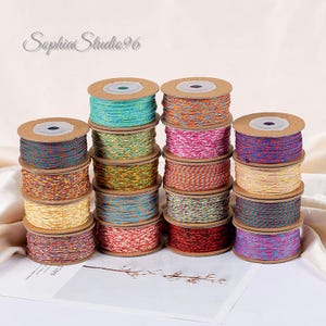 May include: A collection of sixteen spools of multi-colored cord arranged in four stacks. Each spool features a unique blend of vibrant, twisted threads in various color combinations, including blue, green, orange, pink, yellow, and red.