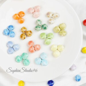Peut inclure: Un assortiment de perles en céramique en forme d'étoile, multicolores, dans des tons d'orange, de rose, de bleu, de marron, de vert et de jaune. Les perles sont disposées sur une assiette blanche. Le texte "Sophia Studio96" est visible.