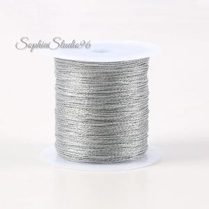 May include: A spool of metallic silver cord wrapped around a white plastic bobbin. The cord has a shimmering, reflective texture and is wound tightly in horizontal layers. The text SophiaStudio96 is visible in the upper left corner.