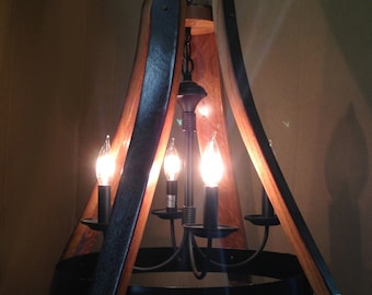 May include: A rustic chandelier with four candle-style lights. The fixture is constructed from dark wood and black metal, with a barrel-inspired design. The light bulbs are lit, casting a warm glow.
