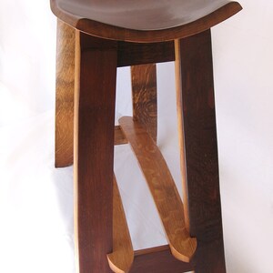 May include: A wooden stool with a curved seat and a unique, angled leg design. The stool is made from dark brown wood with a natural wood finish.