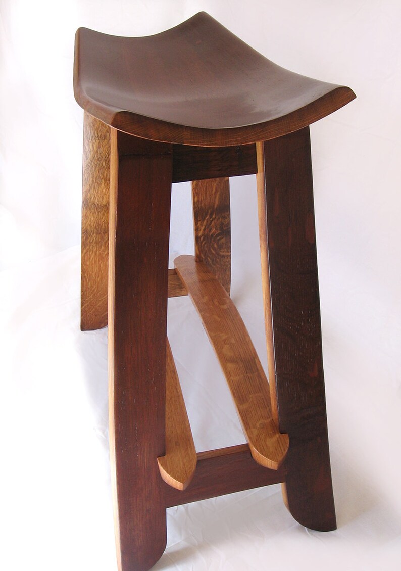 May include: A wooden stool with a curved seat and a unique, angled leg design. The stool is made from dark brown wood with a natural wood finish.