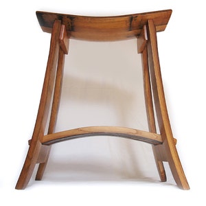 May include: A wooden stool made from repurposed wine barrel staves. The seat is curved and the legs are straight and angled. The stool is made of natural wood with a light brown finish.