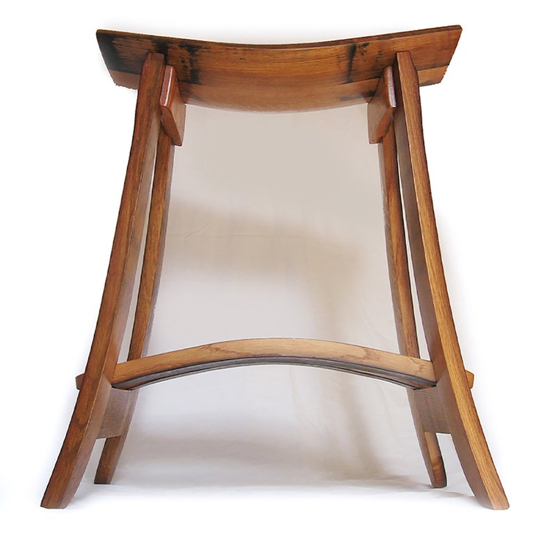 May include: A wooden stool made from repurposed wine barrel staves. The seat is curved and the legs are straight and angled. The stool is made of natural wood with a light brown finish.