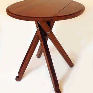 May include: A round wooden table with a folding top and a tripod base. The table is made of dark wood and has a natural finish.