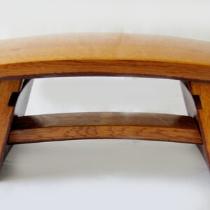 May include: A wooden stool with a curved top and a simple, minimalist design. The stool is made of light brown wood with a natural finish.