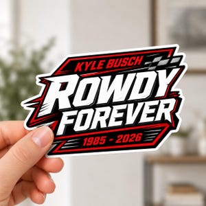May include: A sticker with a black, red, and white design. The text "KYLE BUSCH" is at the top, with "ROWDY FOREVER" in large white letters. The bottom reads "1985-2026". The sticker is held by a hand.