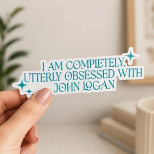 以下が含まれることがあります： 「I AM COMPLETELY, UTTERLY OBSESSED WITH JOHN LOGAN」と書かれた、ターコイズ色の文字が入った白いステッカー。明るいピンクのマニキュアを塗った手でステッカーを持っています。装飾的なスターバーストがテキストを強調しています。