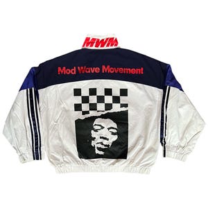 May include: White jacket with blue and black stripes on the sleeves. The jacket has a black and white checkered pattern and a black and white image of a face on the back. The text "Mod Wave Movement" is written in red on the jacket.