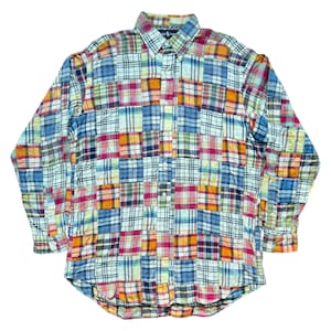 May include: A long-sleeved button-down shirt with a patchwork design. The shirt features a variety of colorful plaid patterns in shades of blue, red, orange, and yellow. The shirt has a classic collar and buttoned cuffs.