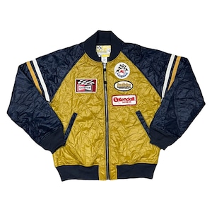 May include: A gold and navy blue quilted bomber jacket with a zip closure. The jacket has several patches on the front, including "Champion", "Kendall Motor Oil", and "Bumblebee".