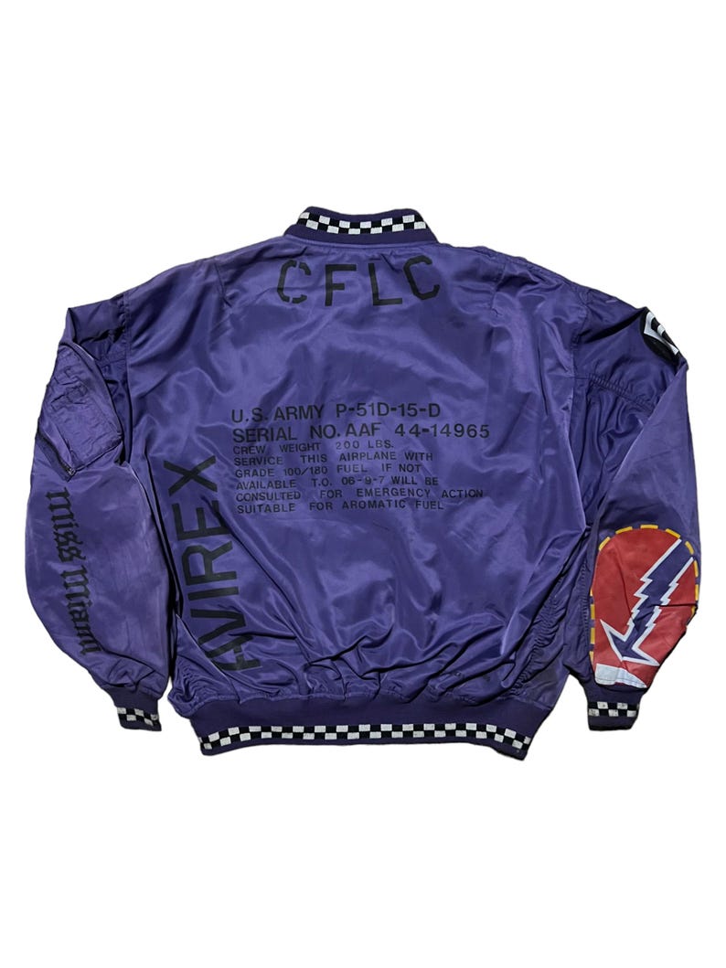 May include: Purple bomber jacket with black and white checkered trim on the collar and cuffs. The back of the jacket features text including "CFLC", "U.S. ARMY P-51D-15-D", and "AVIREX". The left sleeve has "Miss Miant" printed on it, and the right sleeve has a patch with a lightning bolt.