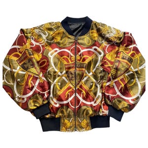 May include: A red, green, and gold bomber jacket with a zipper closure and a patterned design featuring shields and ropes.