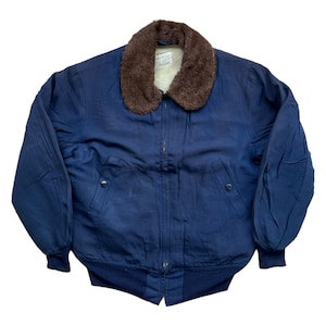 Può includere: Giacca bomber blu navy con colletto in finta pelliccia marrone e orlo e polsini a coste. La giacca ha una chiusura a zip e due tasche anteriori. La fodera interna è bianca.