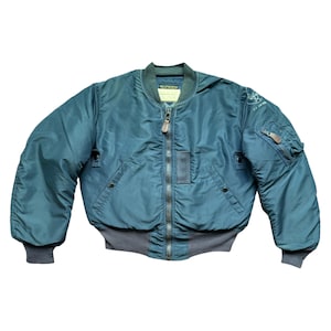 Może przedstawiać: Teal kurtka bomberka z pełnym zapięciem na zamek błyskawiczny, dwiema przednimi kieszeniami oraz prążkowanym szarym dołem i mankietami. Kurtka ma małą naszywkę na górnym lewym rękawie i metkę na kołnierzu. Klasyczny element odzieży wierzchniej.