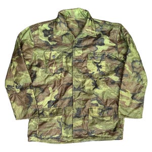 Może przedstawiać: Kurtka w kamuflażu w odcieniach zieleni, brązu i czerni. Kurtka posiada kołnierz, zapięcie na guziki i cztery przednie kieszenie. Kurtka z długim rękawem wykonana jest z lekkiego materiału.