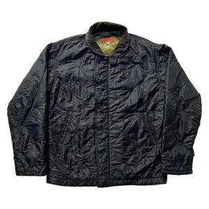 Può includere: Giacca trapuntata nera con colletto in velluto a coste e chiusura con bottoni. La giacca presenta un motivo a rombi e due tasche frontali. Il colletto è marrone e la fodera interna è verde. Stile classico.