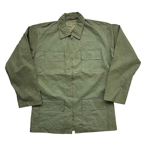 Può includere: Giacca verde oliva con collo, maniche lunghe e chiusura a zip. La giacca presenta quattro tasche frontali e un tessuto strutturato. L'indumento è appoggiato su uno sfondo bianco.