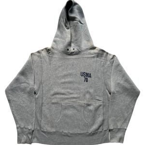 Może przedstawiać: Szara bluza z kapturem ze sznurkiem i kieszenią typu kangur. Tekst "USMA 70" jest wydrukowany w kolorze granatowym na górnej lewej piersi. Bluza ma prążkowane mankiety i dół.