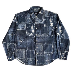 May include: A long-sleeved denim shirt with a patchwork design. The shirt has a button-down front, a collar, and buttoned cuffs. The denim is a dark blue with lighter patches and white stitching details. The shirt has the letters "CC" on the collar.
