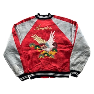 Può includere: Giacca bomber in raso rosso con ricamo di uccelli e motivi floreali. La giacca ha maniche grigie e la scritta "America" ricamata sul retro. Il colletto, i polsini e l'orlo sono neri con strisce bianche.