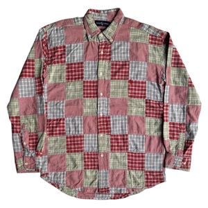 May include: A long-sleeved button-down shirt with a patchwork design. The shirt features a mix of red, white, and green plaid and solid squares. The collar is button-down, and the shirt has a classic fit.