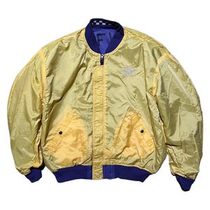 May include: Yellow bomber jacket with a blue collar, cuffs, and hem. The jacket has a zipper closure and two front pockets. The interior is a contrasting blue color. The jacket has the text "FY" and a logo on the chest.