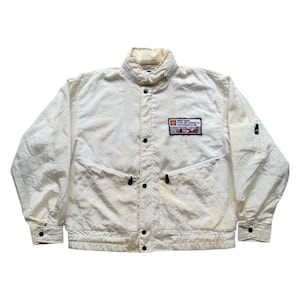 May include: Off-white vintage jacket with a high collar, black buttons, and zippered pockets. A rectangular patch on the chest features text and a small car graphic. The jacket has a slightly textured appearance.