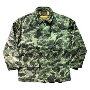Puede incluir: Chaqueta de camuflaje verde y marrón con cuello y forro interior amarillo. La chaqueta tiene cierre de cremallera y dos bolsillos delanteros. La chaqueta tiene un parche en la parte inferior izquierda. La chaqueta es de material acolchado.