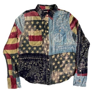 May include: A patchwork button-down shirt featuring various patterns, including the American flag, stars, and paisley designs. The shirt has a collared neckline, buttoned cuffs, and two chest pockets. The color palette includes red, white, blue, and faded yellow.
