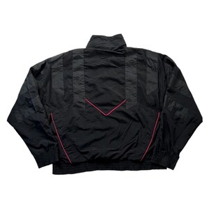 May include: Black vintage windbreaker jacket with a high collar and pink accent lines. The jacket features a chevron design on the back and striped detailing on the sleeves. A classic athletic-inspired outerwear piece.