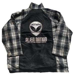 May include: Black and white plaid long-sleeve jacket with a black nylon panel on the back. The nylon panel features an alien head graphic and the text "Alien Nation Long Lasting Rubber Corded".