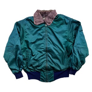 Può includere: Giacca bomber color teal con colletto in ecopelliccia e orlo e polsini a coste blu navy. La giacca ha una chiusura a zip e due tasche anteriori. Un capo di abbigliamento esterno classico.
