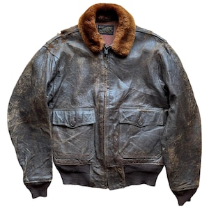 May include: A vintage brown leather bomber jacket with a fur collar. The jacket has two front pockets, a ribbed hem, and cuffs. The leather has a distressed appearance, suggesting age and wear. A classic outerwear piece.