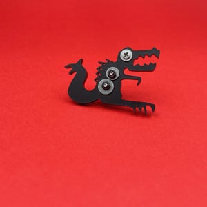 May include: Black metal dinosaur figurine with three silver screws on its back. The dinosaur is posed in a crouching position with its mouth open.