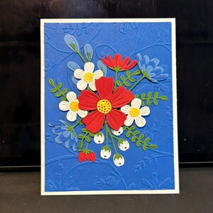 May include: A blue card with a white border features a 3D floral design. The flowers are red, white, and blue. The background is a blue textured pattern.