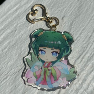 May include: A green-haired anime character with blue eyes wearing a pink and green dress with a blue ribbon. The character is surrounded by pink flowers and green leaves. The image is on a clear acrylic keychain with a gold metal clasp.