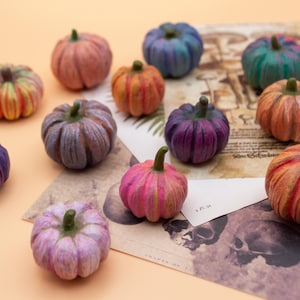May include: A collection of miniature pumpkins in various colors, including orange, purple, pink, and green. Each pumpkin has a green stem and is arranged on a vintage paper background. The pumpkins are likely for fall or Halloween decor.