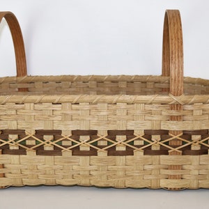 May include: A large oval-shaped woven basket with two wooden handles. The basket has a brown and green geometric pattern around the middle. A can of V8 juice is next to the basket for size comparison.