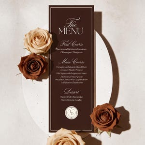 May include: A tall, rectangular dark brown menu card with white text and a thin white border. The menu lists courses including Burrata, Duck, Filet Mignon, Salmon, and Cheesecake. Four roses in shades of cream and brown surround the card.