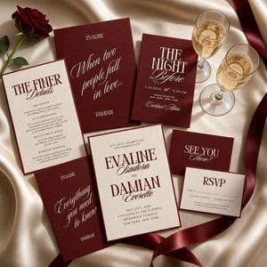 Könnte beinhalten: Ein Hochzeitspapeterie-Set mit dunkelroten und cremefarbenen Karten in eleganter Serifenschrift und Schreibschrift. Das Set enthält eine Einladung für Evaline Isadora und Damian Everette, eine Antwortkarte und Informationskarten, arrangiert mit einer roten Rose und zwei Sektgläsern.